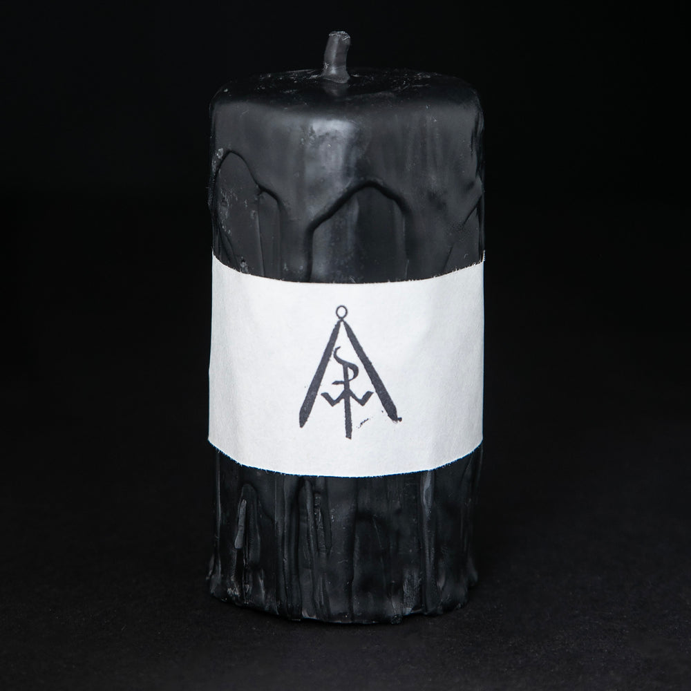 Short black beeswax pillar candle by RITUAALIA on black background. The candle has a rustic textured finish with visible drips.