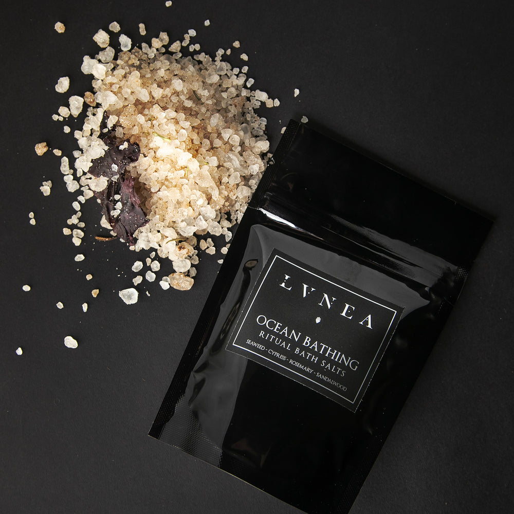 4oz black resealable pouch of LVNEA's Ocean Bathing bath salts with a mound of clay-hued and seaweed-speckled salt next to it