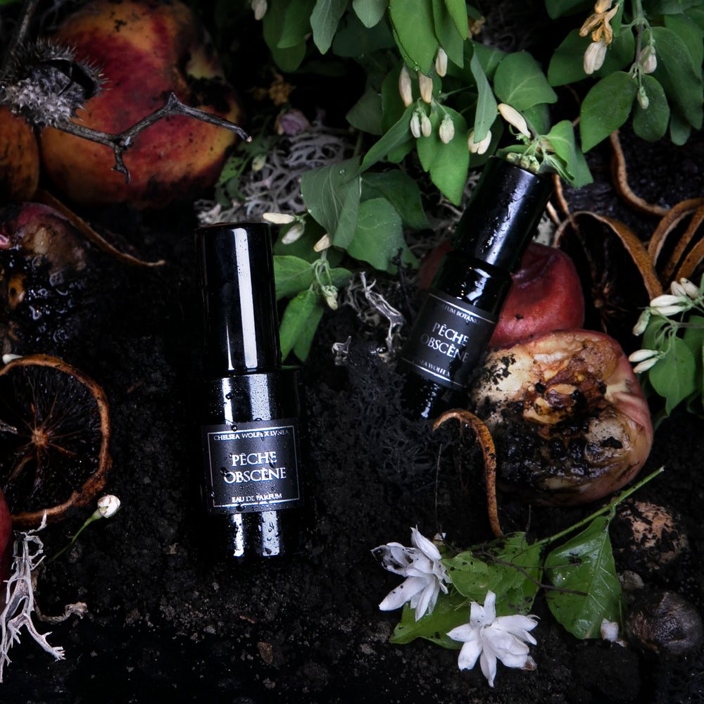 
                      
                        30ml eau de parfum and 10ml parfum botanique bottles of Pêche Obscène. The two bottles are lying on dirt surrounded by ripe peaches, jasmine, and botanicals
                      
                    