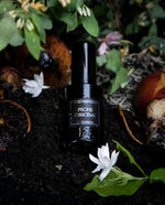 30ml black glass bottle of LVNEA best-selling natural perfume Peche Obscene lying on dirt surrounded by ripe peaches, jasmine, and botanicals