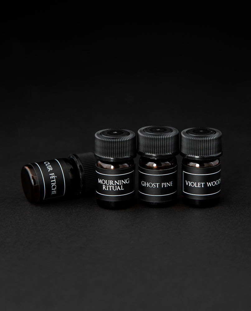 Four 1.25 ml sample vials of LVNEA's oil perfume on black background. Shown are Cuir Fétiche, Mourning Ritual, Ghost Pine, and Violet Woods