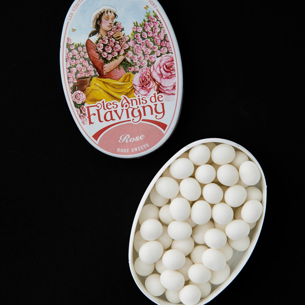 Open tin of rose flavoured bonbons. There is an illustration of a woman in a field of roses on the top of the tin.