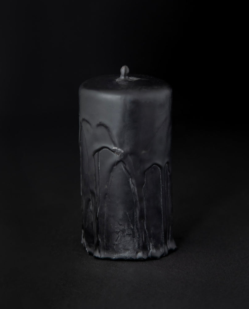 Black beeswax pillar candle by RITUAALIA with label removed, revealing the candle's rustic textured finish.