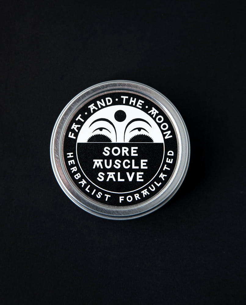 2oz metal tin of Fat and the Moon's "Sore Muscle Salve" seen from above. The label is black and white with an illustration of a half moon on it.